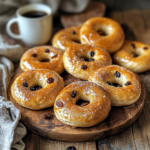 A batch of freshly baked soft and sweet bagels on a wooden board, some topped with cinnamon sugar and others with a shiny honey glaze, styled with a linen napkin and a cup of coffee in the background.